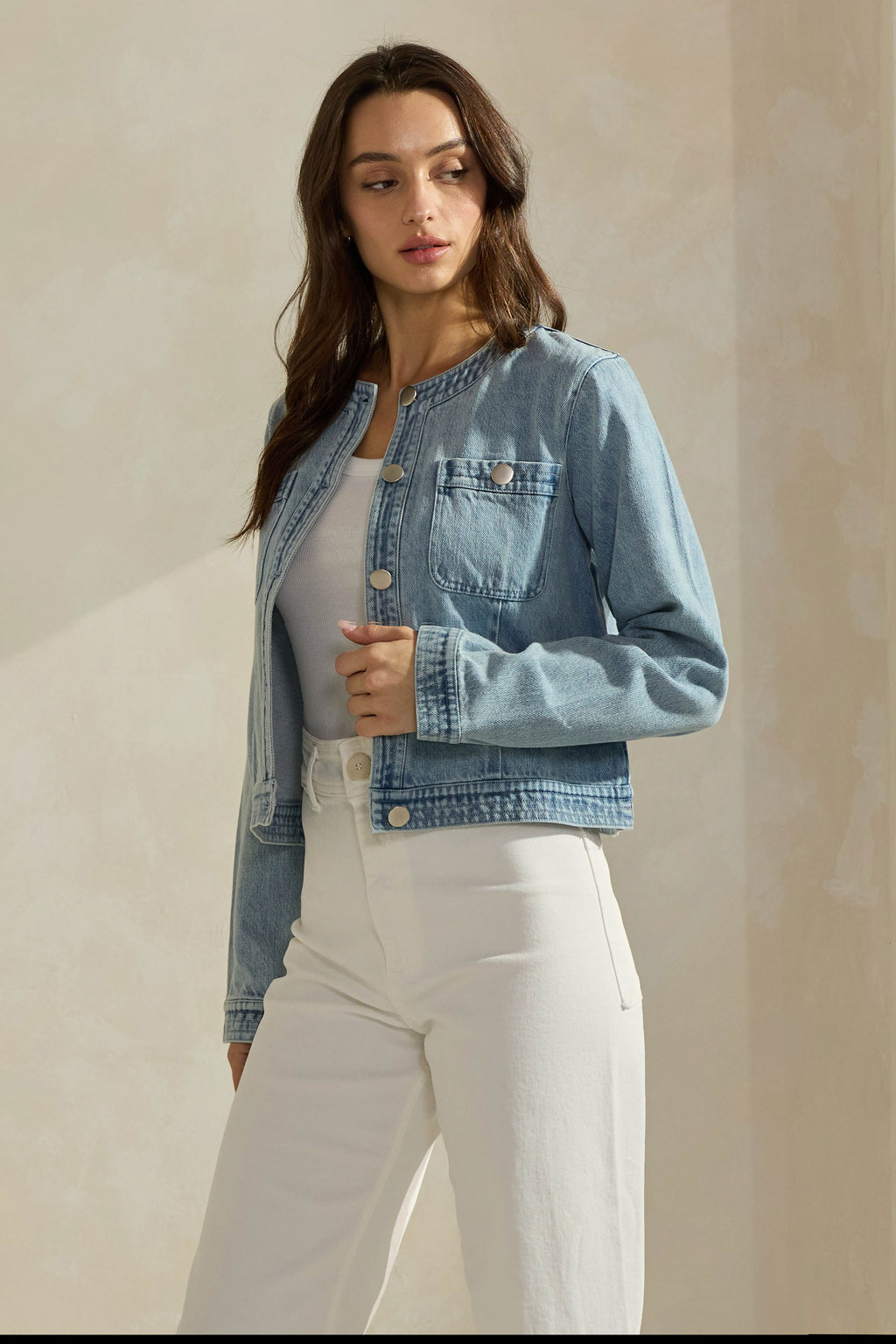 Woman wearing a light washed denim jean jacket on a neutral background