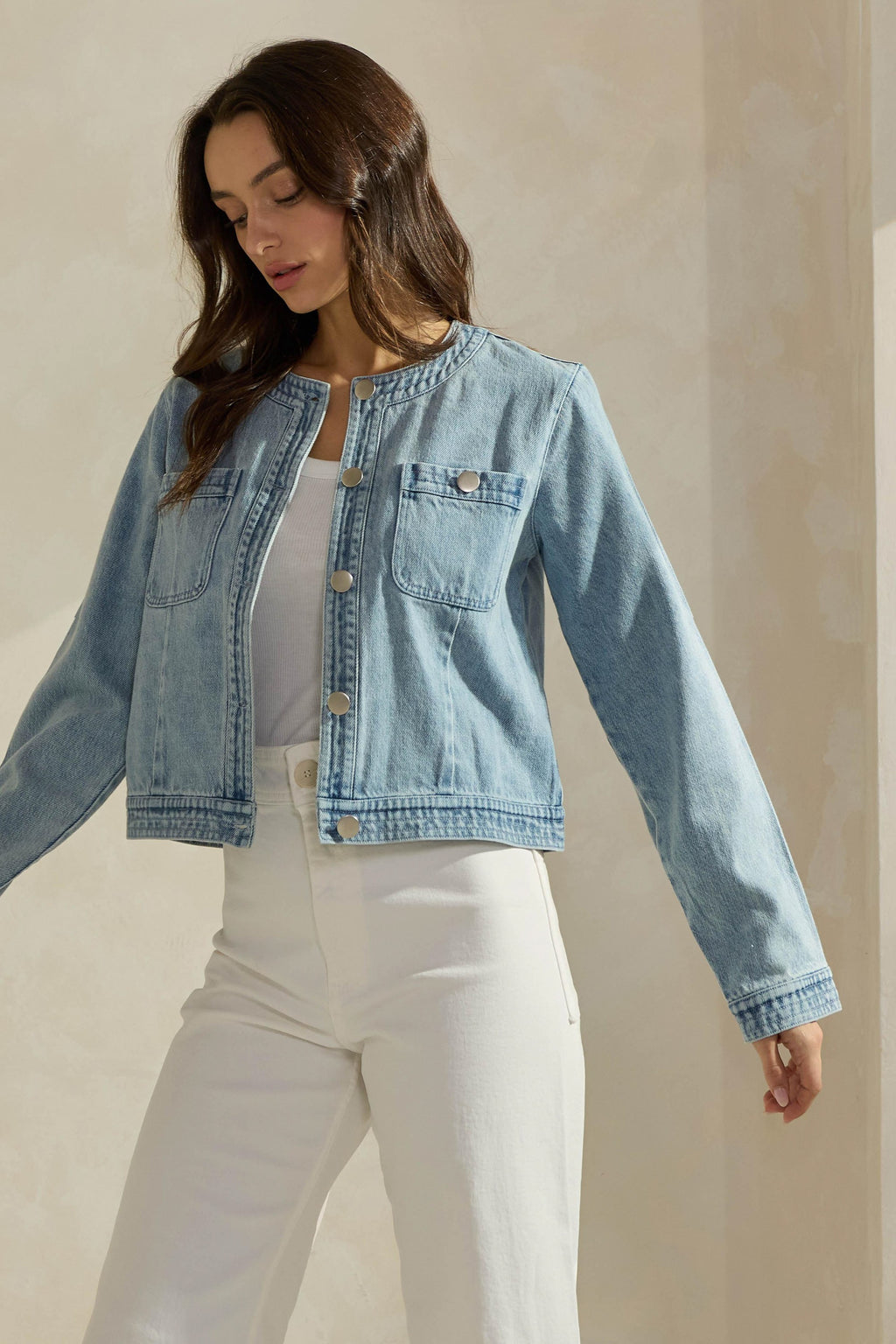 Woman wearing a light washed denim jean jacket on a neutral background