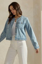Woman wearing a light washed denim jean jacket on a neutral background