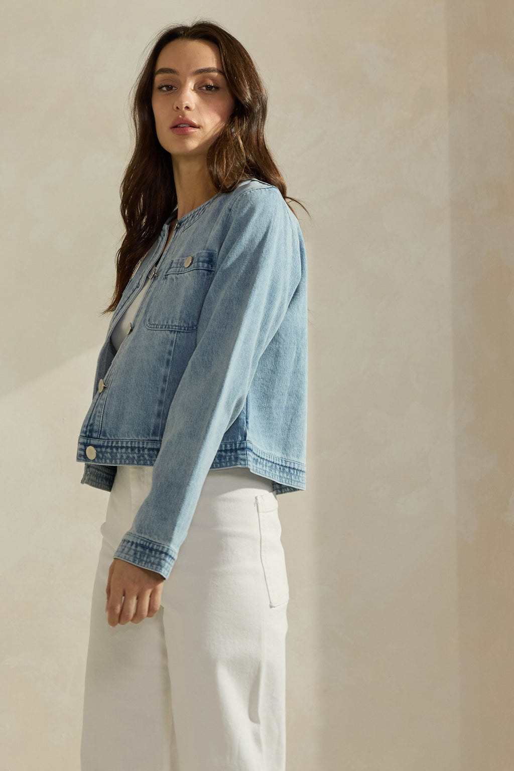 Woman wearing a light washed denim jean jacket on a neutral background