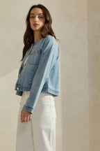 Woman wearing a light washed denim jean jacket on a neutral background