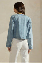 Back view of a woman wearing a light washed denim jean jacket on a neutral background