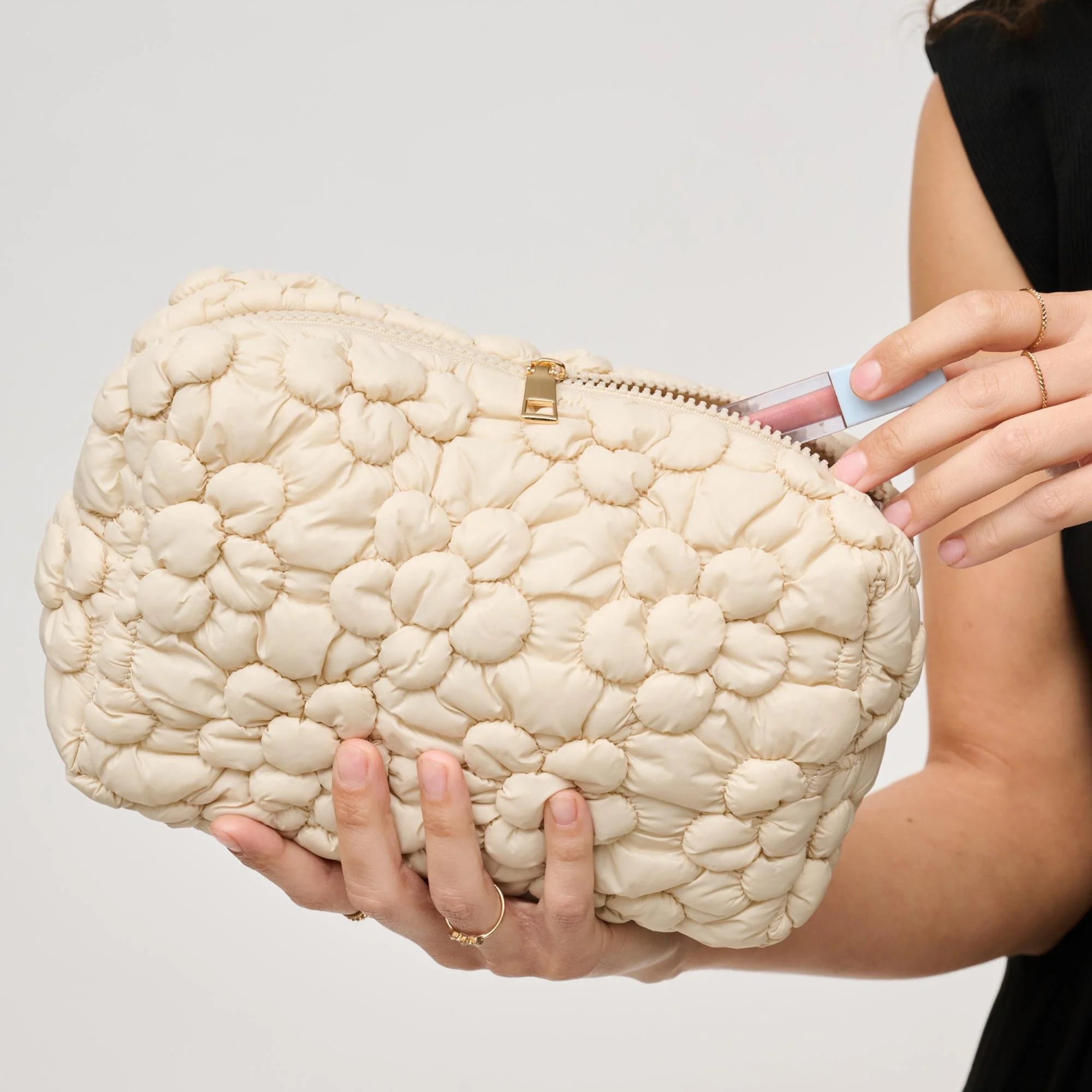 Cream-colored quilted floral design cosmetic bag with a gold zipper on a white background