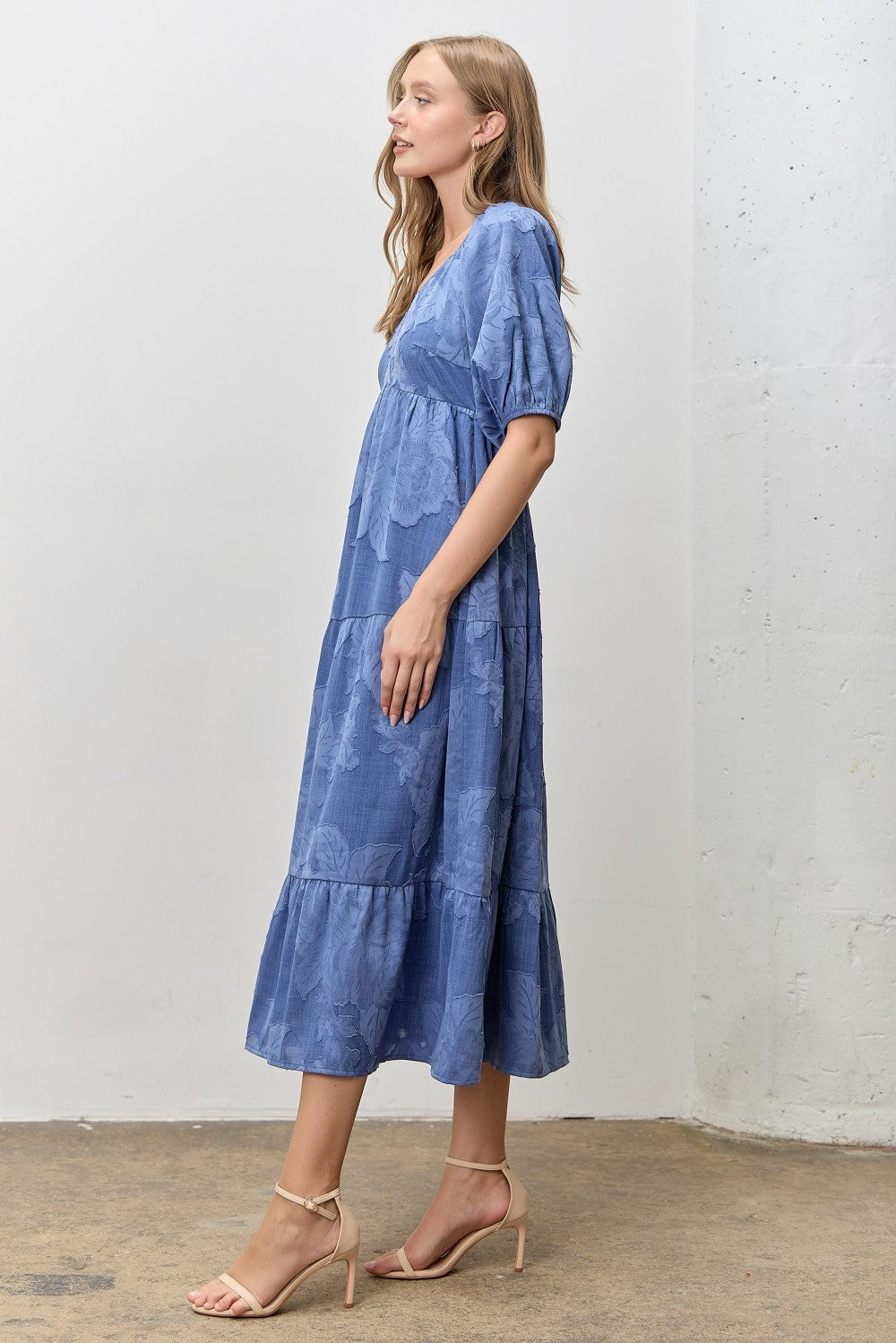 Woman wearing a blue jacquard tiered midi dress against a white wall.
