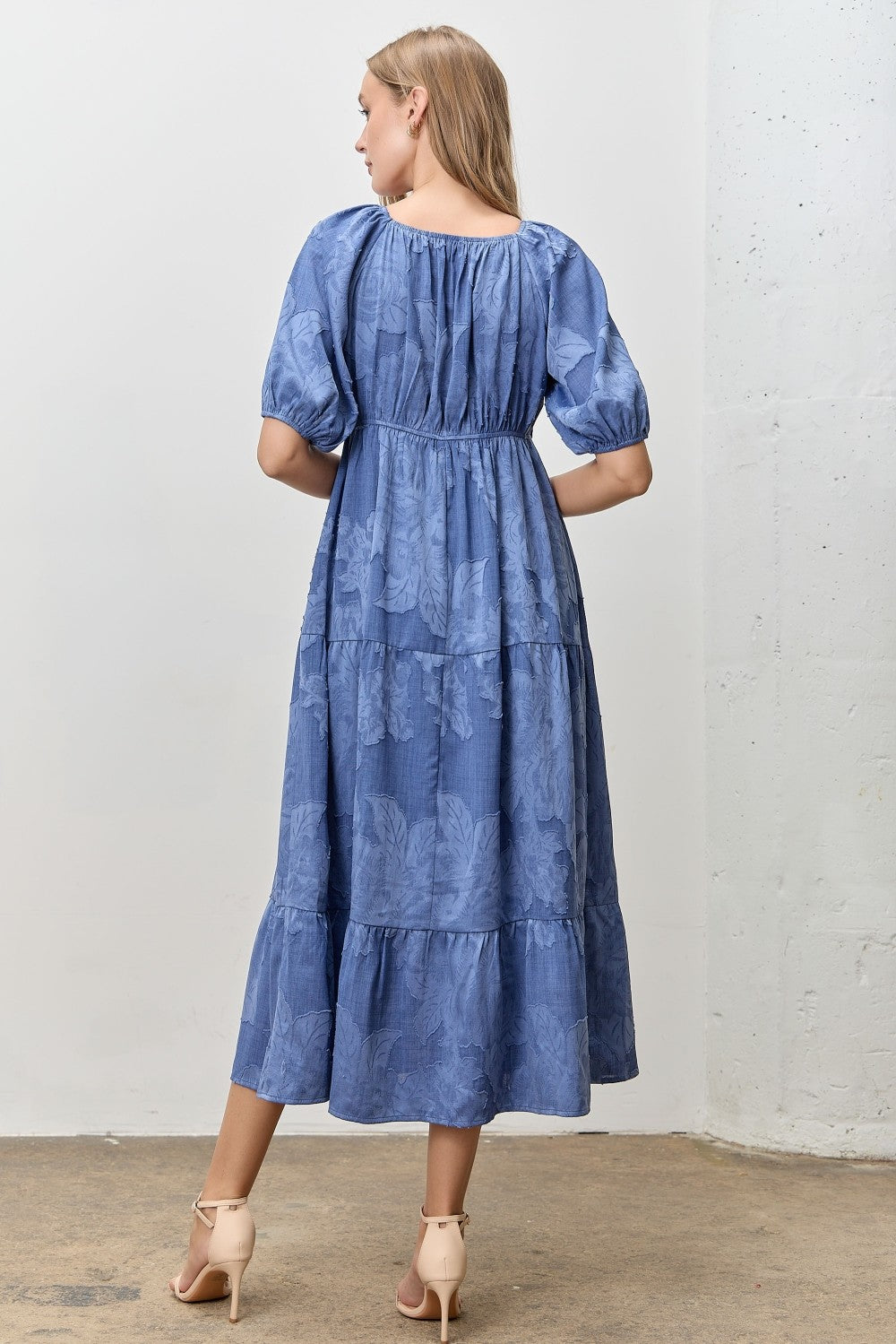 Woman wearing a blue jacquard tiered midi dress against a white wall.