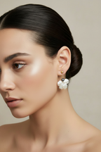 Woman wearing flower dangle dark gray pearl accent earrings against a neutral background