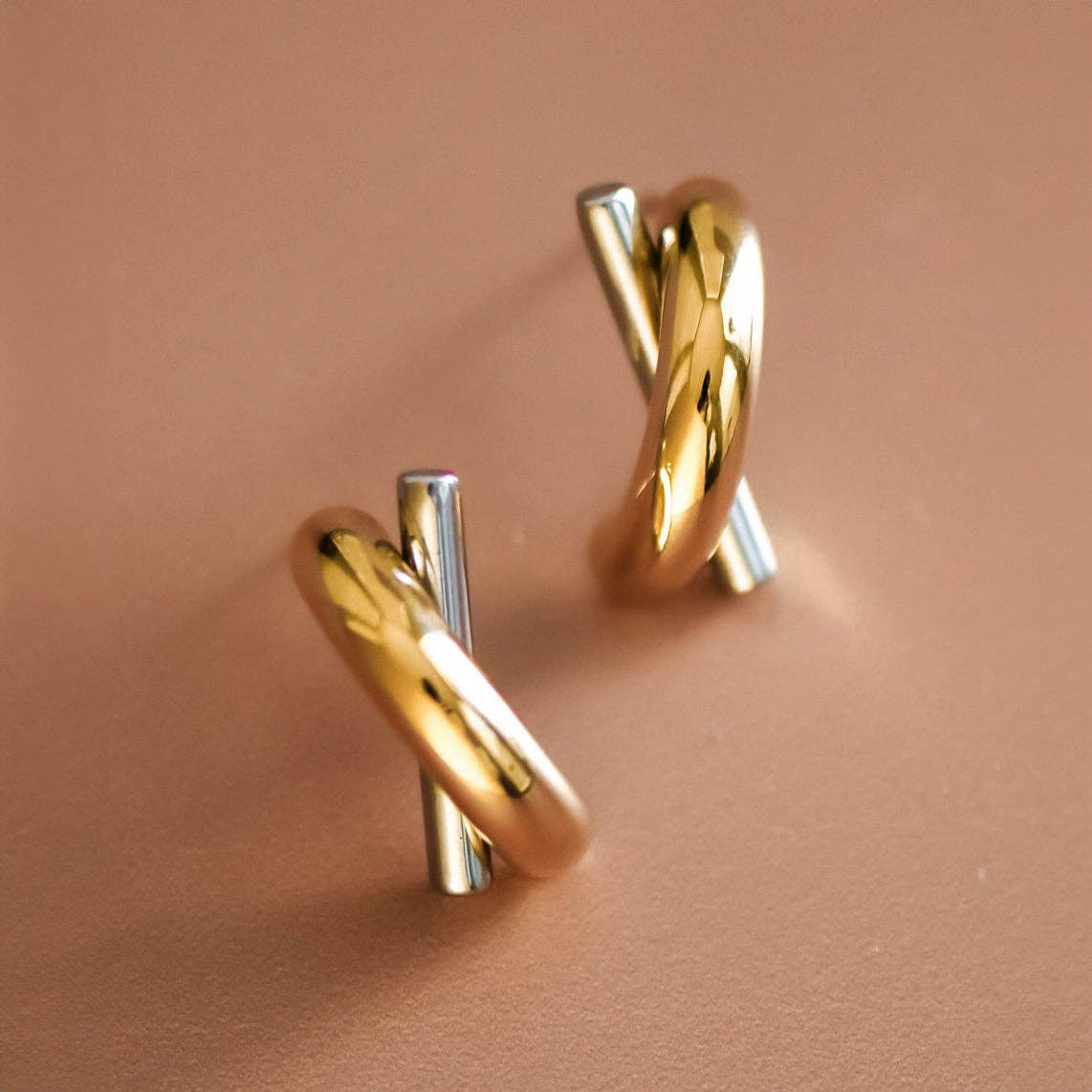 Gold and silver tone criss cross earrings on a pink background