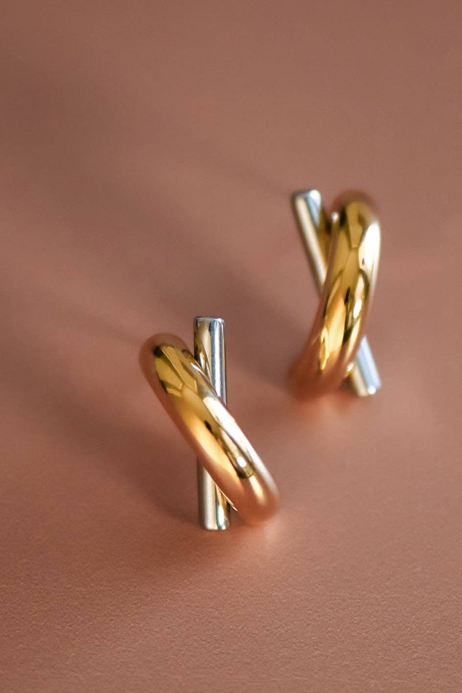 Gold and silver criss cross hoop earrings on a pink background