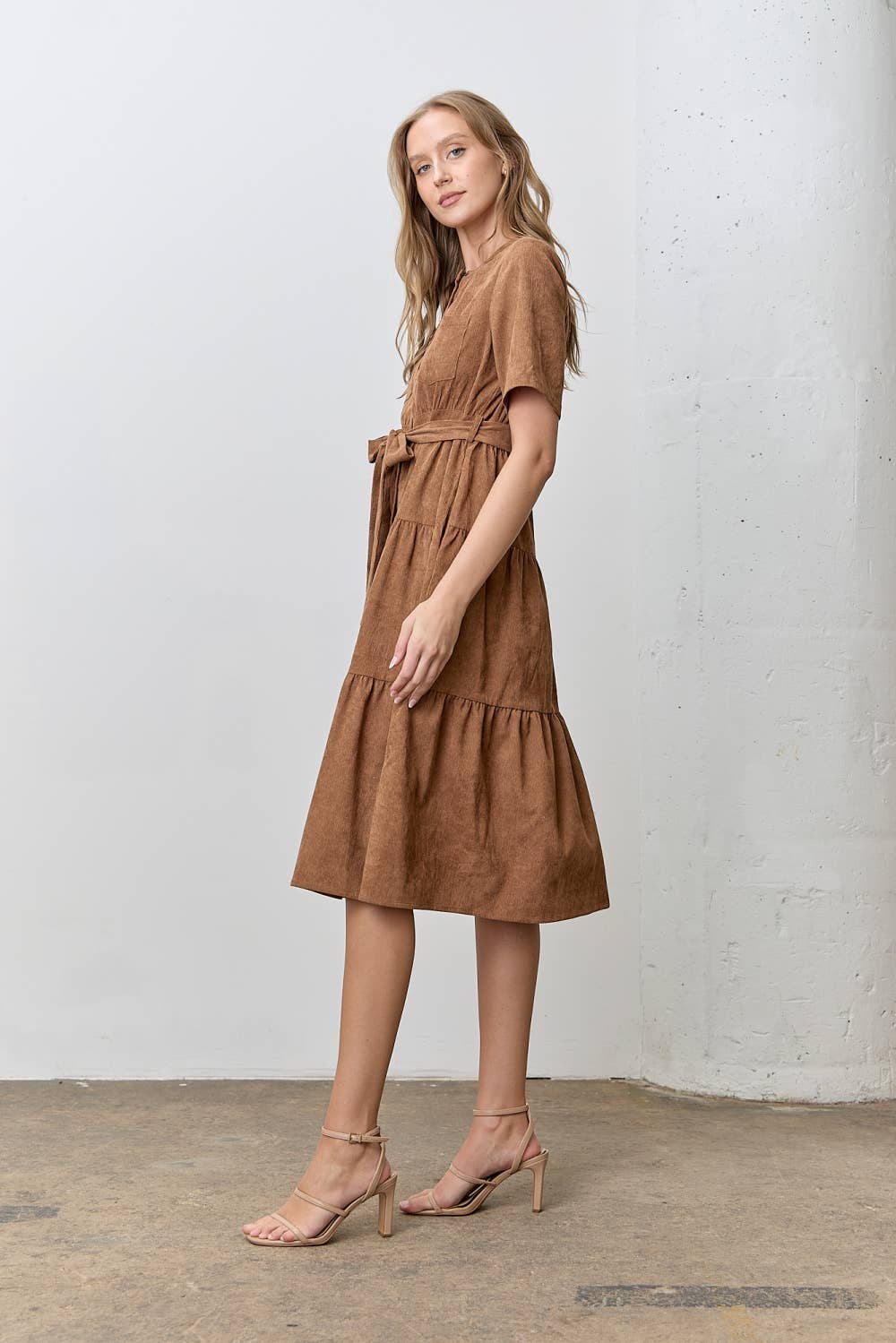 Woman wearing a brown corduroy tiered dress standing against a white wall.