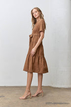 Woman wearing a brown corduroy tiered dress standing against a white wall.