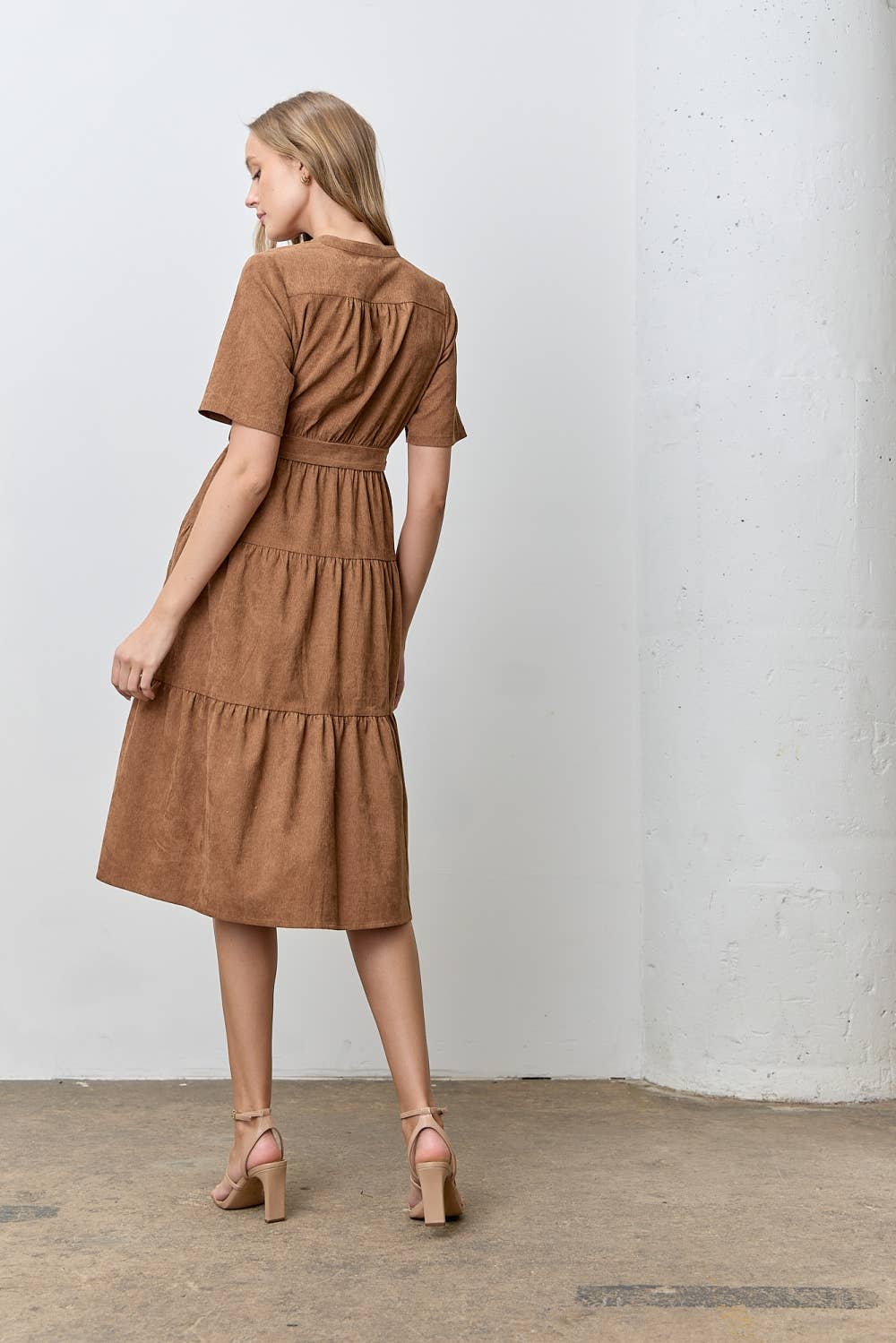 Woman wearing a brown corduroy tiered dress against a white wall