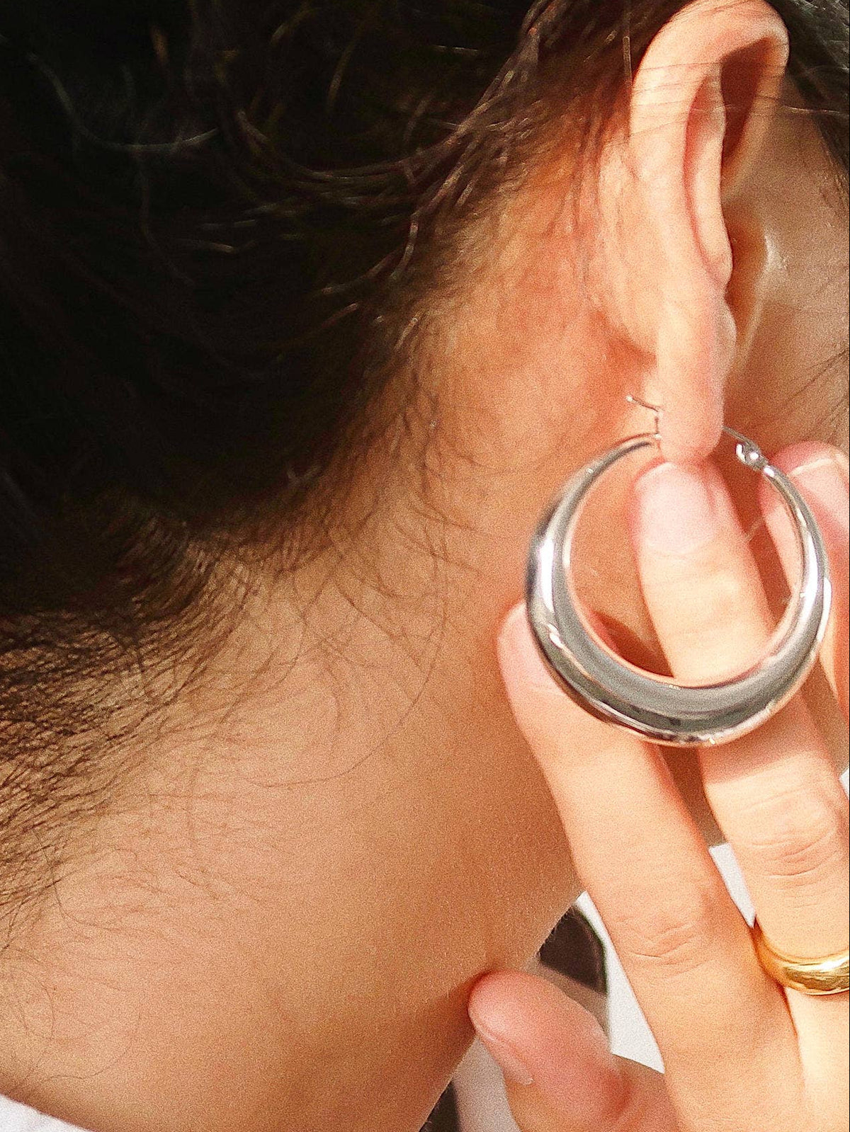 Woman wearing a polished silver-plated hoop earrings with a thick, rounded crescent shape