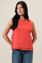 Woman wearing an orange sleeveless layered top and blue jeans on a beige background