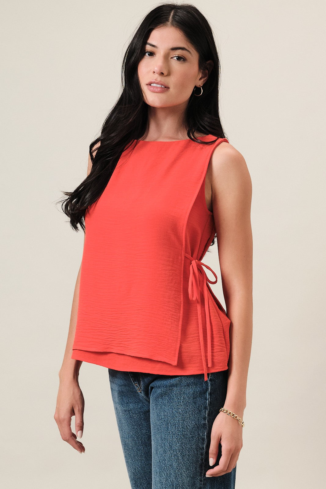Woman wearing an orange sleeveless layered top and blue jeans on a beige background