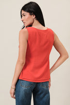 Back view of a woman wearing an orange sleeveless layered top and blue jeans on a beige background