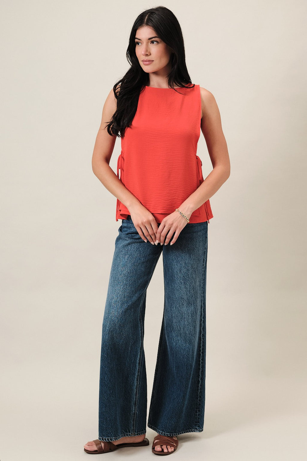 Woman wearing an orange sleeveless layered top and blue jeans on a beige background