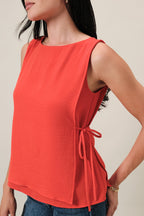 Woman wearing an orange sleeveless layered top and blue jeans on a beige background