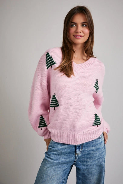 Woman wearing a pink sweater with green Christmas tree patterns on a plain background