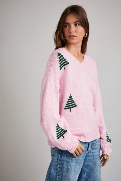 Woman wearing a pink sweater with green Christmas tree patterns on a plain background