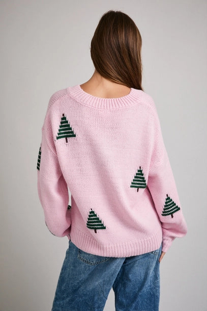 Back view of woman wearing a pink sweater with green Christmas tree patterns on a plain background