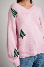 Woman wearing a pink sweater with green Christmas tree patterns on a plain background