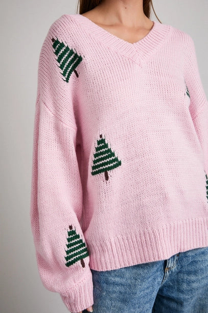 Woman wearing a pink sweater with green Christmas tree patterns on a plain background