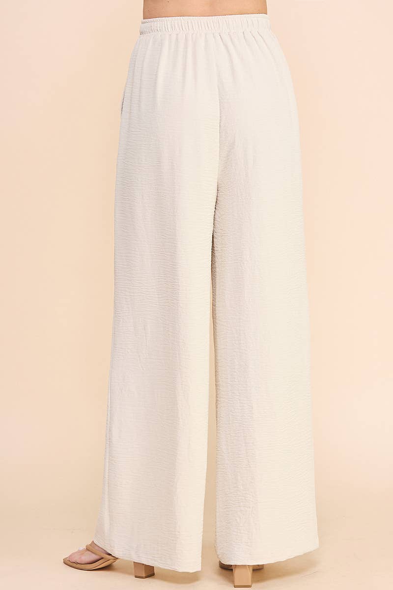 Back view of a woman wearing oatmeal wide leg pants on a beige background