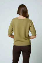 Back view of a woman wearing an olive sweater top and brown shorts on a light gray background