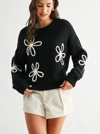 Woman wearing a black sweater with white daisy loop appliques on a white background