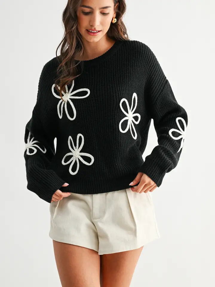 Woman wearing a black sweater with white daisy loop appliques on a white background