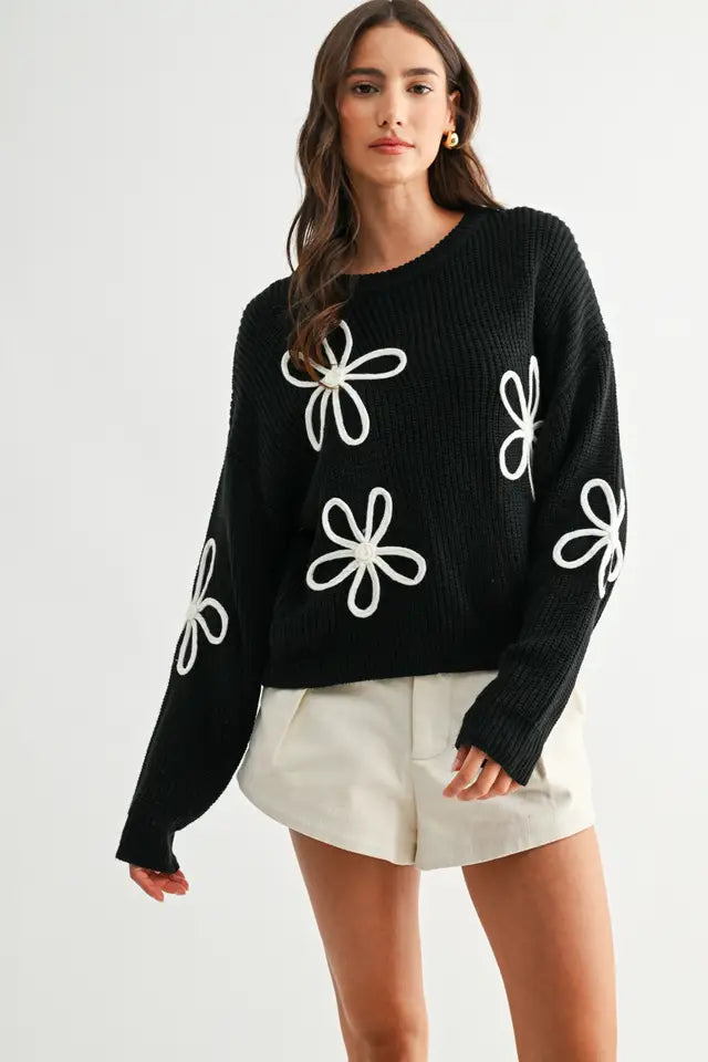 Woman wearing a black sweater with white daisy loop appliques on a white background