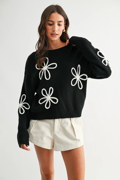Woman wearing a black sweater with white daisy loop appliques on a white background