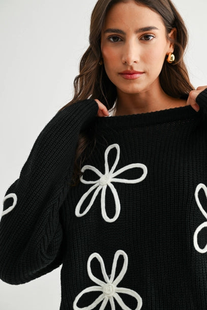 Woman wearing a black sweater with white daisy loop appliques on a white background