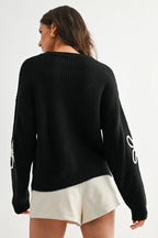 Back view of a woman wearing a black sweater with white daisy loop appliques on a white background