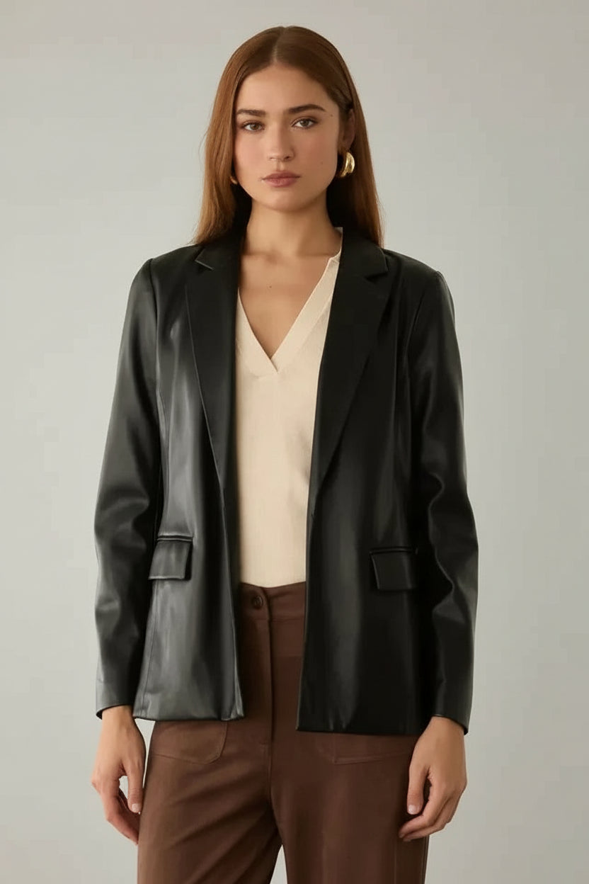 Woman wearing a black faux leather jacket over a beige top and brown pants in a neutral setting.