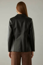 Back view of woman wearing a black faux leather jacket and brown pants in a neutral setting.