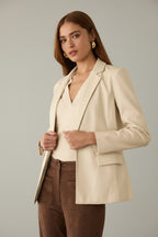 Woman wearing an ivory blazer and brown pants against a neutral background