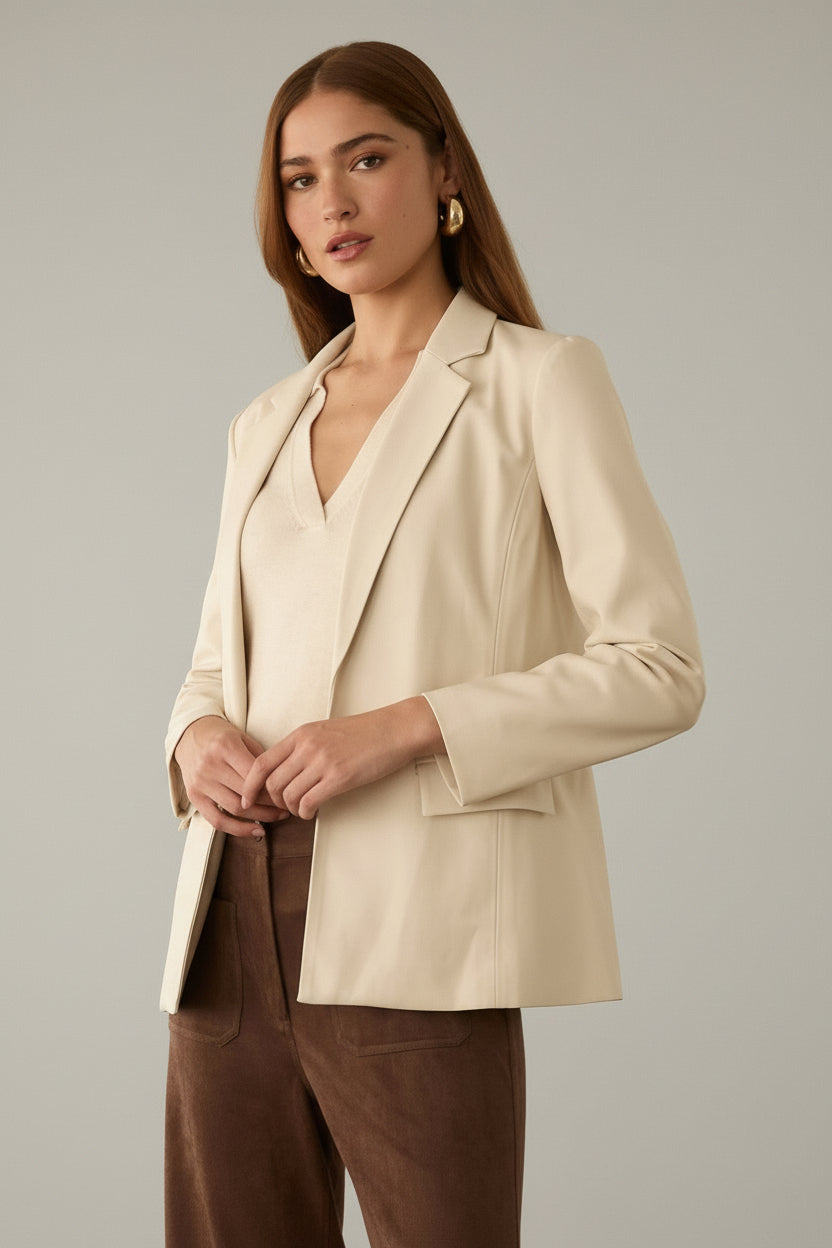 Woman wearing an ivory blazer and brown pants against a neutral background