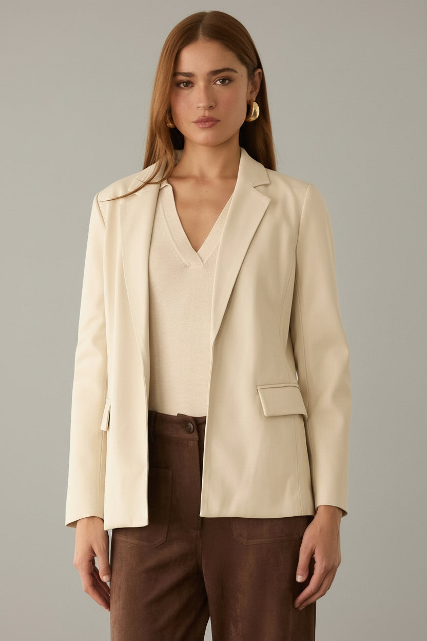 Woman wearing an ivory blazer and brown pants against a neutral background