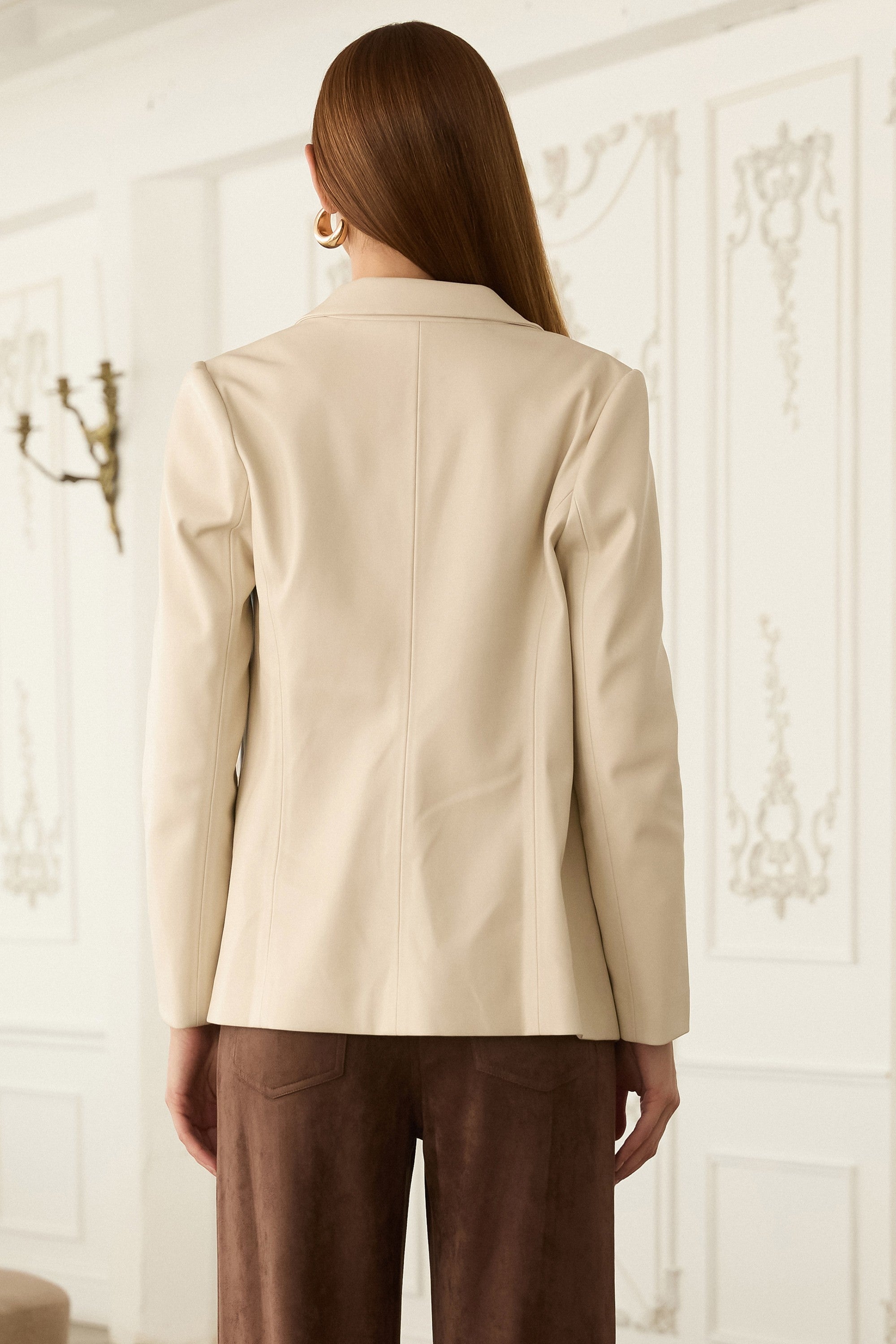 Back view of a woman wearing an ivory blazer and brown pants against a neutral background