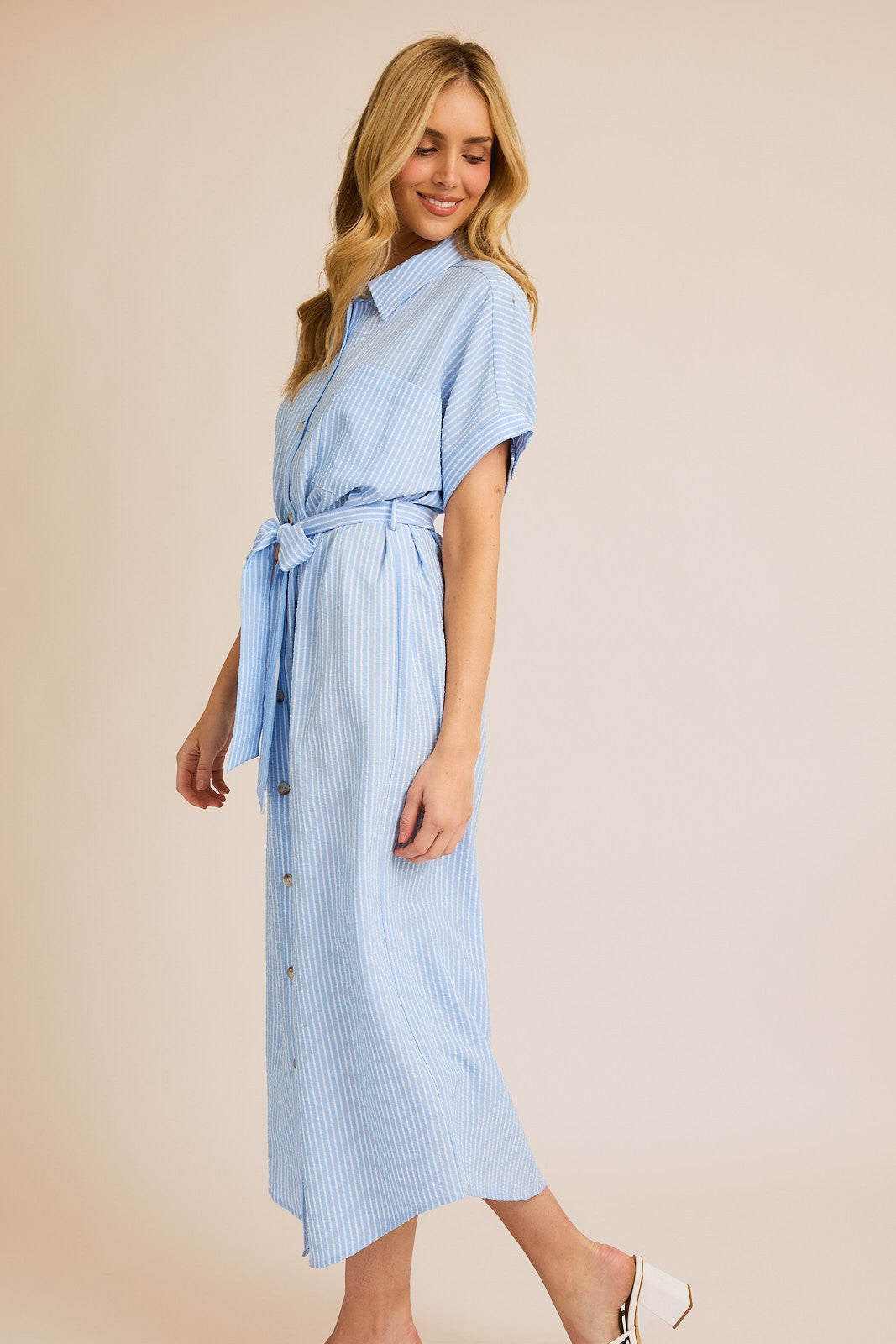Woman wearing striped button down shirt dress against beige background