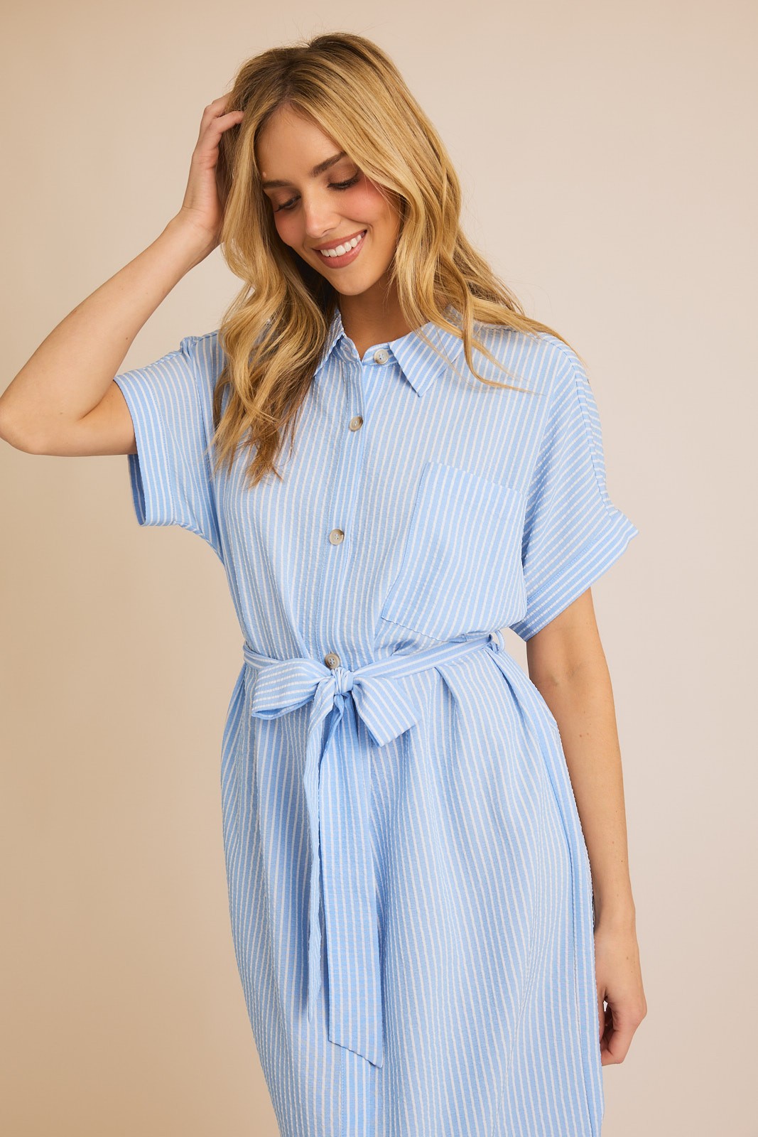 Woman wearing striped button down shirt dress against beige background