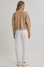 Back view of a woman wearing a open cardigan with long sleeves, front pockets and detail stitching and white pants against a white background