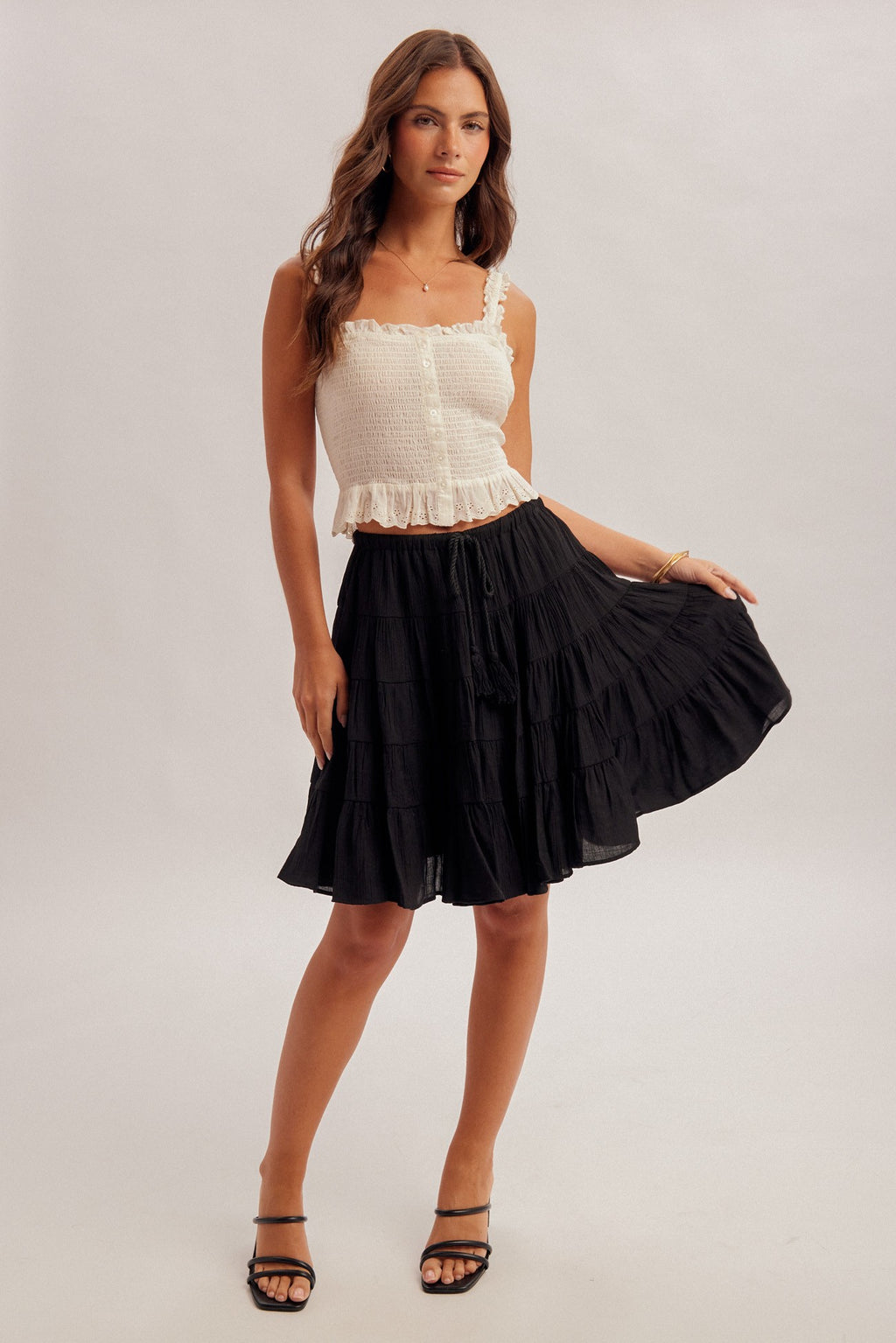 Black tiered skirt with elastic and tie waist and white top worn by a woman on a plain background
