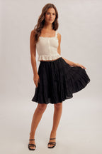 Black tiered skirt with elastic and tie waist and white top worn by a woman on a plain background
