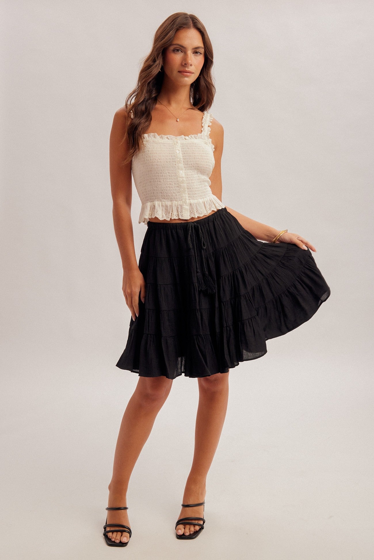 Black tiered skirt with elastic and tie waist and white top worn by a woman on a plain background