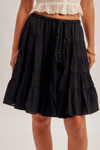 Black tiered skirt with elastic and tie waist worn by a woman on a plain background