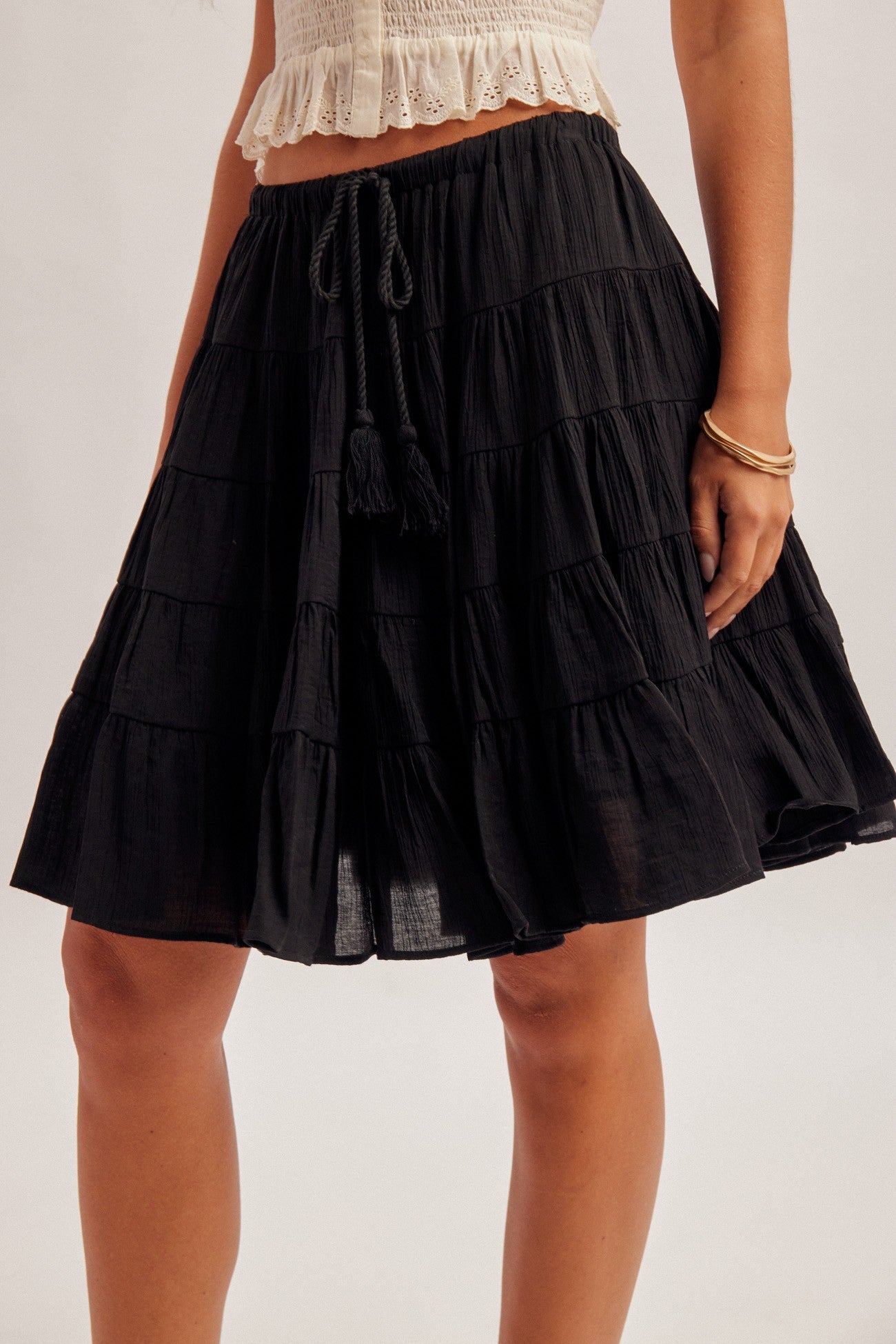 Black tiered skirt with elastic and tie waist worn by a woman on a plain background