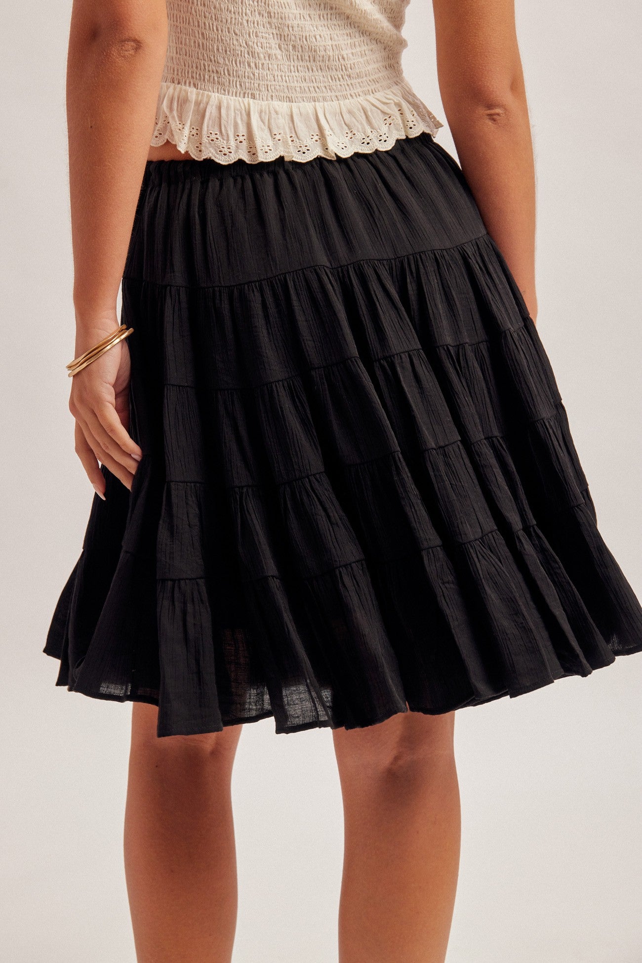 Back view of a women wearing a black tiered skirt with elastic and tie waist on a plain background