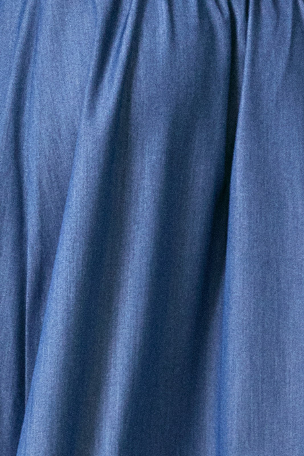 A close-up of denim blue fabric with a soft, slightly textured surface and gentle folds.